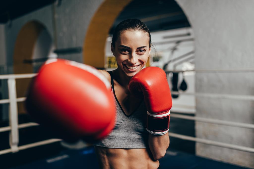 Young female boxer in gloves training and smiling